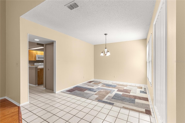 unfurnished dining area featuring light tile patterned floors, a textured ceiling, and a notable chandelier