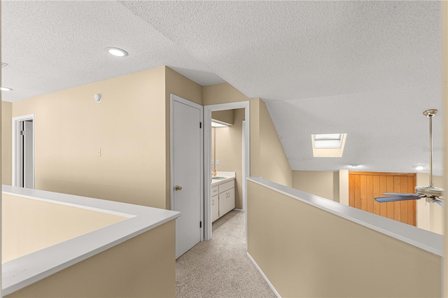 hall with a textured ceiling, sink, lofted ceiling with skylight, and light carpet