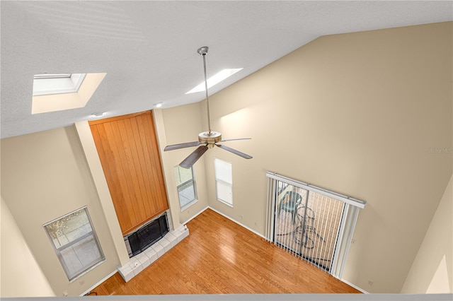 unfurnished living room with ceiling fan, light hardwood / wood-style flooring, lofted ceiling with skylight, a textured ceiling, and a tiled fireplace