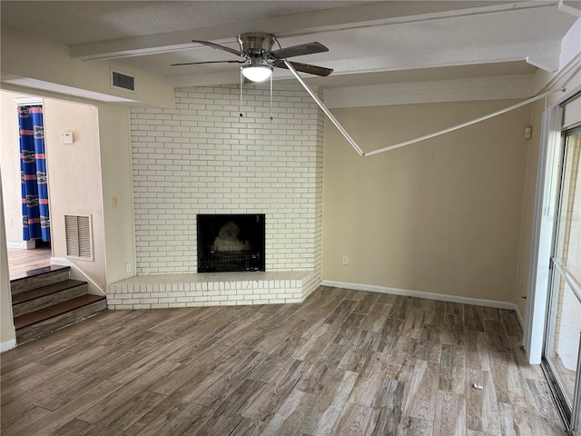 unfurnished living room featuring a brick fireplace, a textured ceiling, ceiling fan, hardwood / wood-style floors, and vaulted ceiling with beams