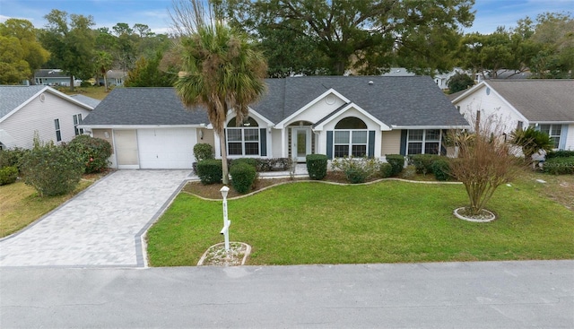 ranch-style home featuring decorative driveway, roof with shingles, an attached garage, and a front lawn