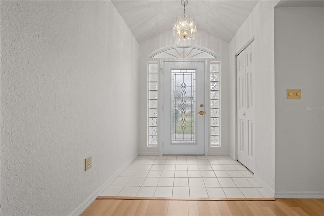 entrance foyer with a textured wall, vaulted ceiling, light wood-style flooring, and baseboards