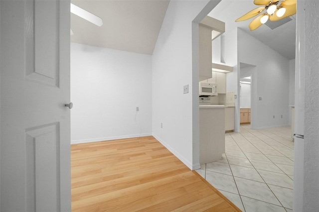 interior space with lofted ceiling, ceiling fan, visible vents, baseboards, and light wood-type flooring