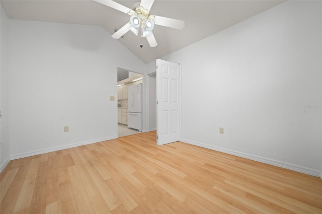 unfurnished bedroom featuring lofted ceiling, freestanding refrigerator, light wood-style flooring, and baseboards