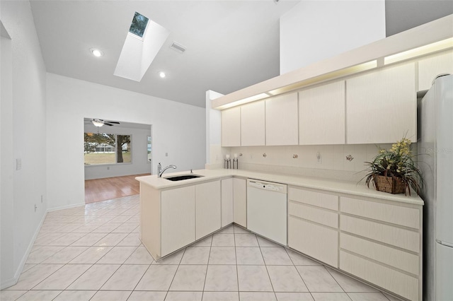 kitchen with white appliances, light tile patterned floors, a peninsula, light countertops, and a sink