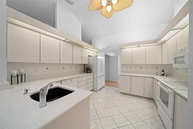 kitchen with white appliances, decorative backsplash, vaulted ceiling, light countertops, and a sink