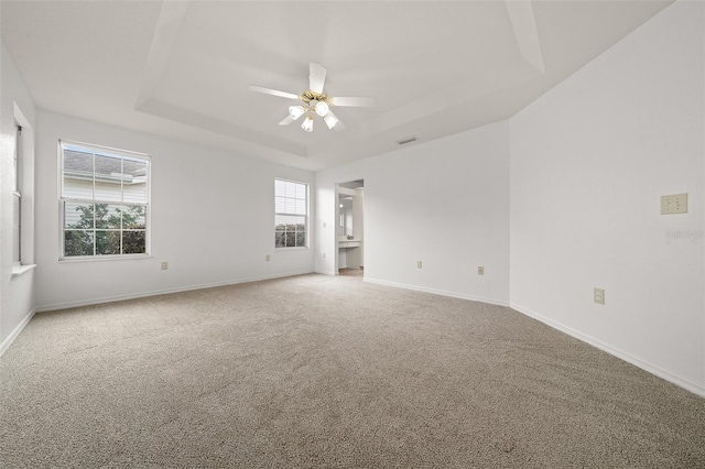 carpeted empty room featuring visible vents, baseboards, a raised ceiling, and a ceiling fan