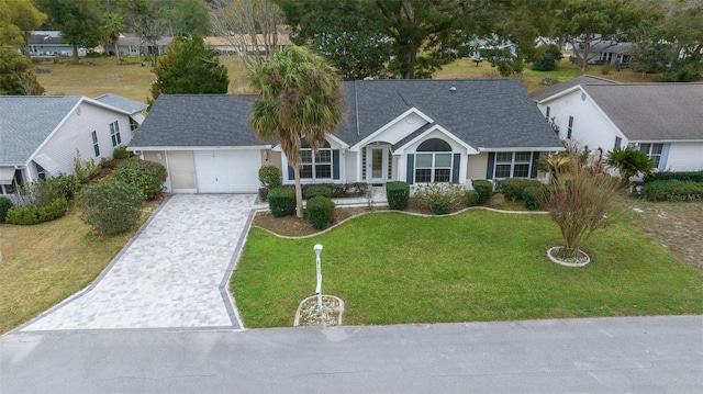 view of front of property featuring a garage, a shingled roof, decorative driveway, and a front yard