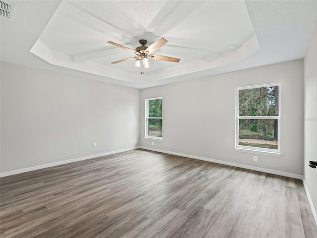 unfurnished room with wood-type flooring, a textured ceiling, a raised ceiling, and ceiling fan