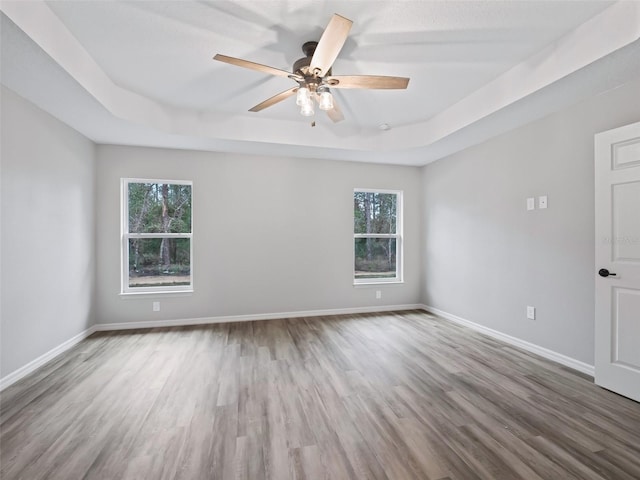 empty room featuring hardwood / wood-style flooring, ceiling fan, and a raised ceiling