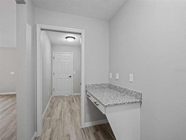 corridor with light wood-type flooring and a textured ceiling