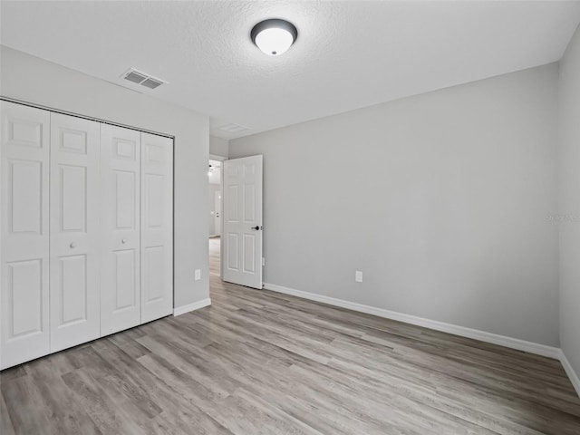 unfurnished bedroom featuring a textured ceiling, light hardwood / wood-style flooring, and a closet