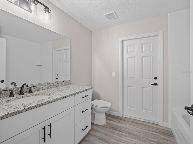 bathroom featuring vanity, wood-type flooring, a textured ceiling, and toilet