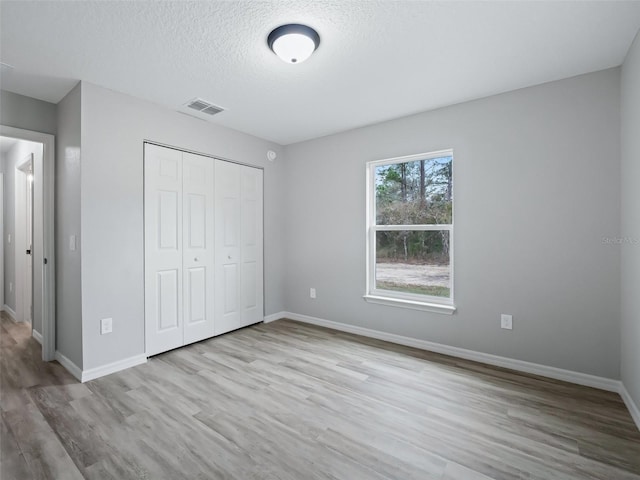 unfurnished bedroom with a closet, a textured ceiling, and light wood-type flooring