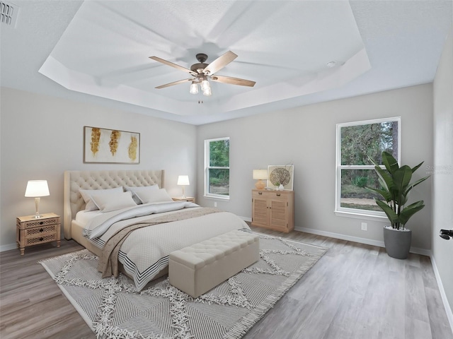 bedroom featuring ceiling fan, light hardwood / wood-style floors, and a raised ceiling