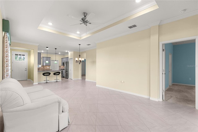 tiled living room featuring ceiling fan with notable chandelier, crown molding, and a tray ceiling