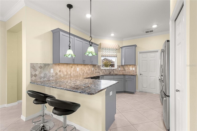 kitchen with gray cabinetry, a breakfast bar, sink, stainless steel refrigerator, and hanging light fixtures