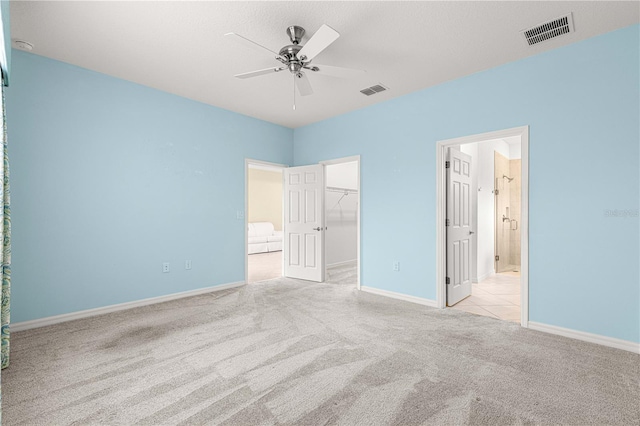 unfurnished bedroom featuring a walk in closet, ceiling fan, connected bathroom, light colored carpet, and a closet