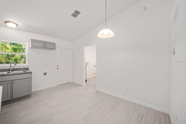 interior space with high vaulted ceiling, sink, gray cabinets, decorative light fixtures, and light hardwood / wood-style floors