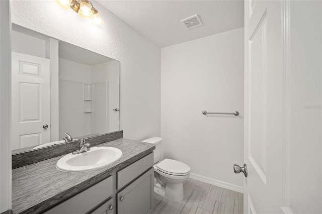 bathroom featuring a textured ceiling, vanity, toilet, and walk in shower