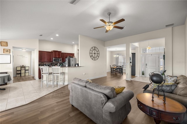 living room featuring ceiling fan with notable chandelier, light hardwood / wood-style floors, and vaulted ceiling