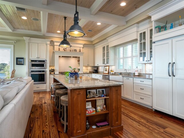 kitchen featuring pendant lighting, a center island, light stone countertops, appliances with stainless steel finishes, and white cabinetry