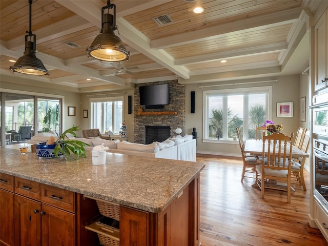 kitchen featuring pendant lighting, plenty of natural light, light stone countertops, and light hardwood / wood-style flooring