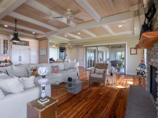 living room with ceiling fan, a stone fireplace, beamed ceiling, hardwood / wood-style floors, and wood ceiling