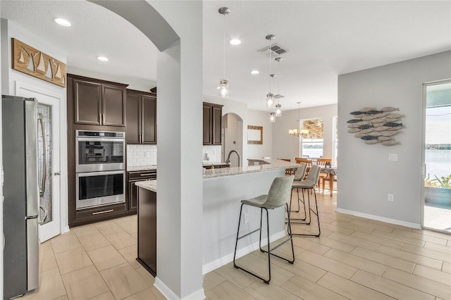 kitchen featuring visible vents, arched walkways, dark brown cabinetry, appliances with stainless steel finishes, and backsplash