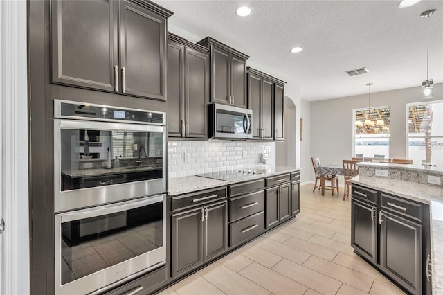 kitchen featuring light stone counters, visible vents, an inviting chandelier, stainless steel appliances, and decorative backsplash