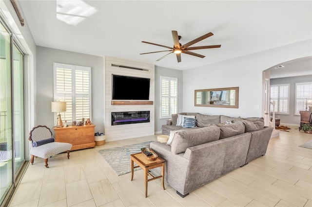 living room featuring a large fireplace, arched walkways, and a ceiling fan