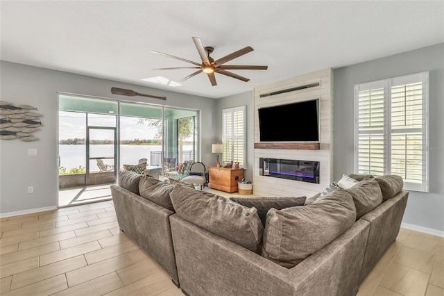 living area featuring light wood-style flooring, baseboards, ceiling fan, and a fireplace