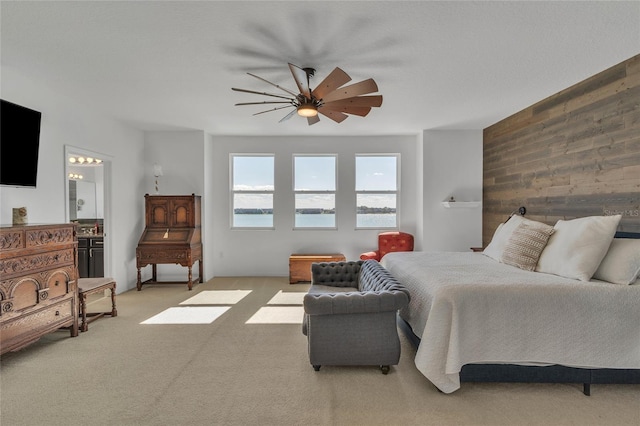 bedroom with wooden walls, light colored carpet, ensuite bathroom, and a ceiling fan