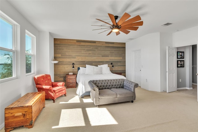 bedroom with light carpet, wooden walls, an accent wall, and ceiling fan