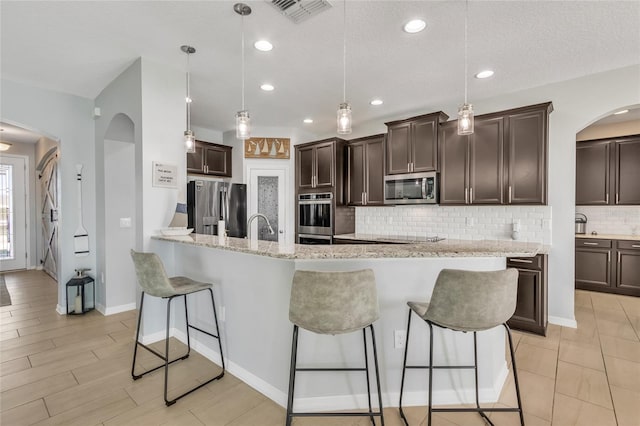 kitchen featuring visible vents, a breakfast bar, arched walkways, dark brown cabinetry, and appliances with stainless steel finishes