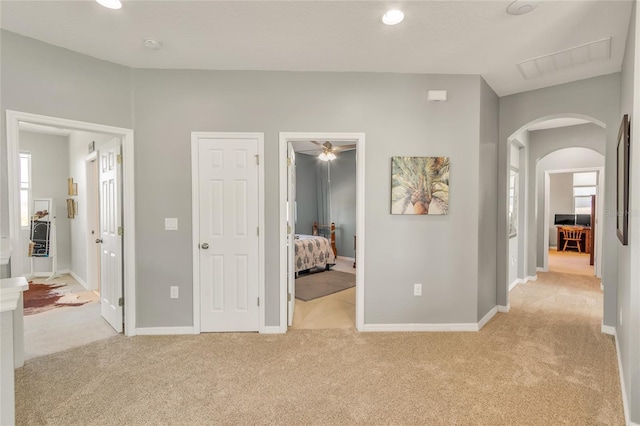 corridor with arched walkways, light colored carpet, and baseboards