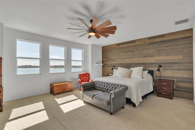 bedroom with visible vents, light carpet, a water view, wood walls, and ceiling fan