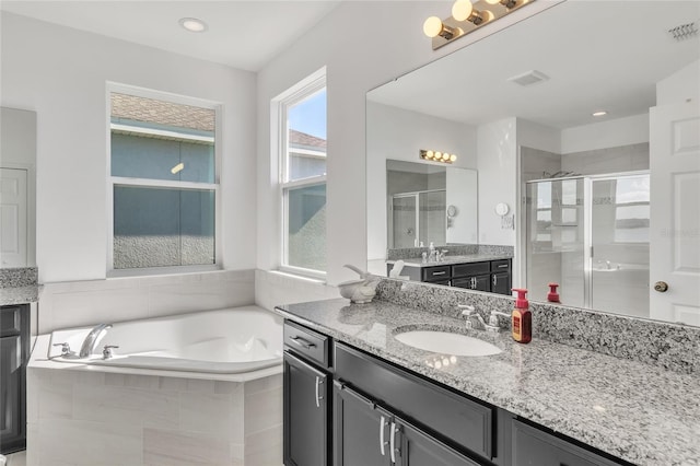 full bath with visible vents, a garden tub, two vanities, a stall shower, and a sink