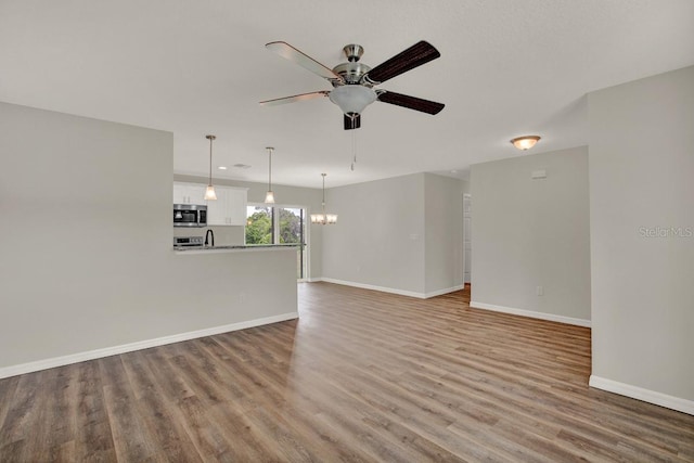 unfurnished living room with ceiling fan with notable chandelier and light wood-type flooring