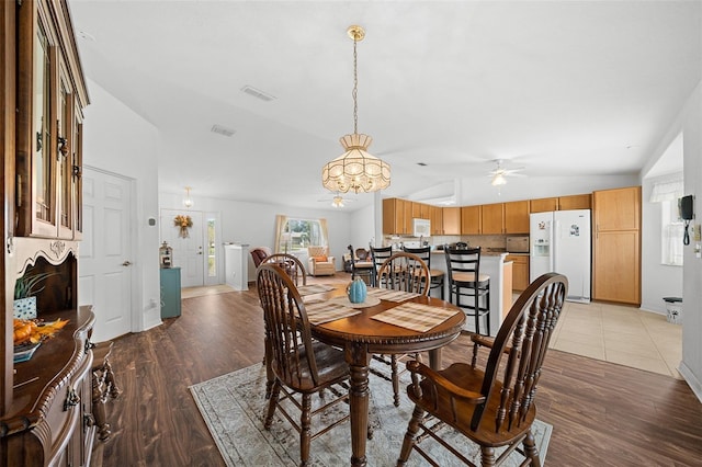 dining space with ceiling fan with notable chandelier, wood-type flooring, and vaulted ceiling