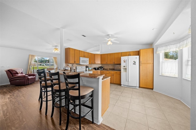 kitchen with lofted ceiling, white appliances, a kitchen breakfast bar, light hardwood / wood-style flooring, and decorative backsplash