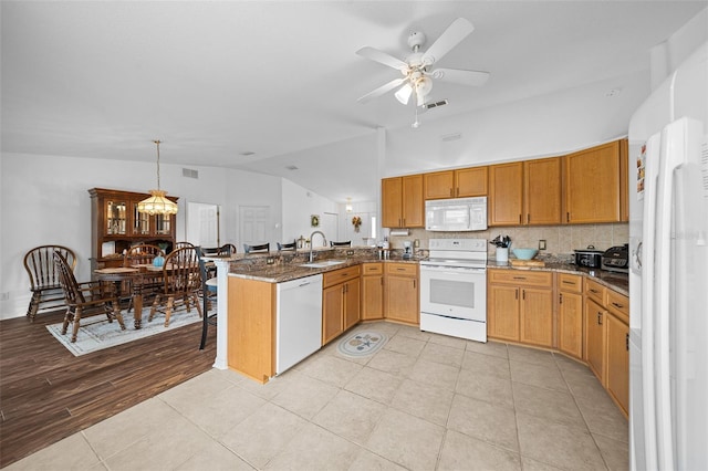 kitchen featuring kitchen peninsula, dark stone counters, vaulted ceiling, decorative light fixtures, and white appliances