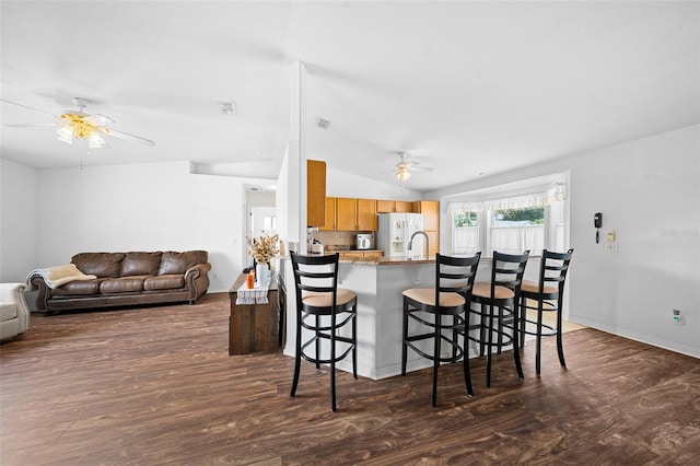 kitchen featuring a breakfast bar area, kitchen peninsula, dark wood-type flooring, and lofted ceiling