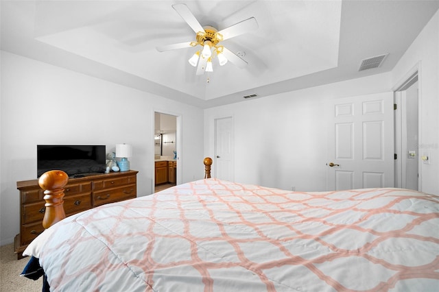 bedroom featuring a raised ceiling, connected bathroom, ceiling fan, and carpet floors