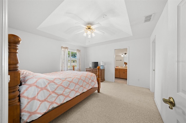 bedroom featuring a tray ceiling, ensuite bath, ceiling fan, and light carpet