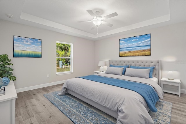 bedroom with a raised ceiling, ceiling fan, and light hardwood / wood-style floors