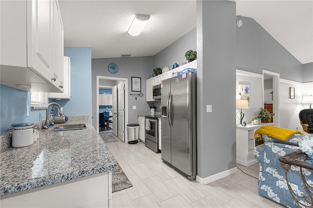 kitchen with lofted ceiling, white cabinets, sink, appliances with stainless steel finishes, and light stone counters