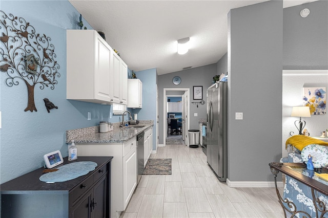 kitchen with white cabinetry, sink, light stone countertops, vaulted ceiling, and appliances with stainless steel finishes