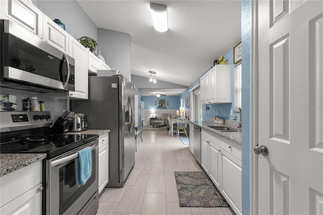 kitchen with sink, vaulted ceiling, appliances with stainless steel finishes, light stone counters, and white cabinetry