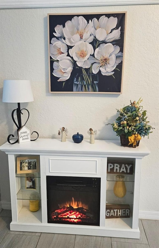 room details with a warm lit fireplace, a textured wall, and wood finished floors